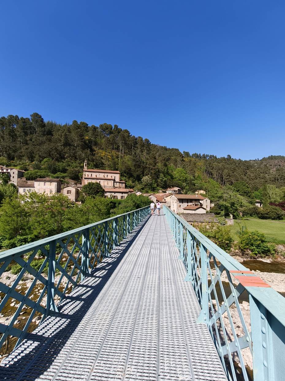Passerelle métallique verte menant au village, sous un ciel bleu