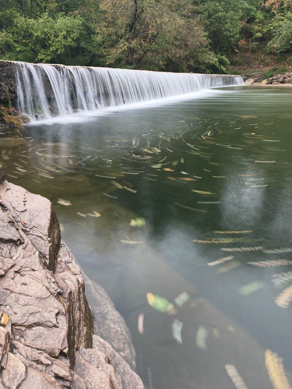 Seuil en pierre sur la rivière, eau lisse et rochers au premier plan